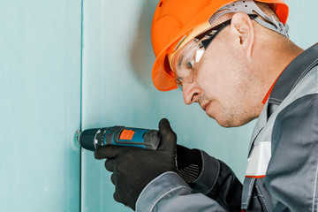 A male construction worker screws a screw with an electric screwdriver. Concept of repair and construction