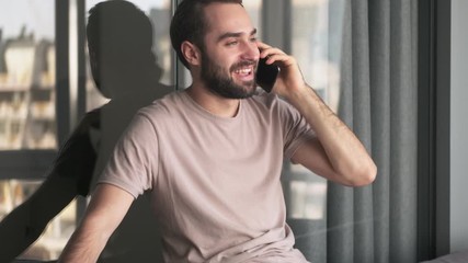 Sticker - A handsome young man is talking on his smartphone sitting at home in the living room