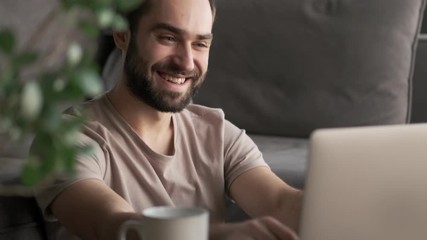 Wall Mural - A handsome young man is typing on his laptop computer while sitting at home in the living room