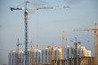 © Dilya - Inside place for many tall buildings under construction and cranes under a blue sky working on place with tall homes