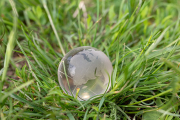 earth planet symbol on background of green grass. glass ball on nature backdrop. ecology concept, en