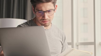 Wall Mural - Handsome young concentrated man indoors at home using laptop computer