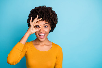 Canvas Print - Portrait of excited astonished afro american girl show okay sign make binoculars watch look impressed scream wow omg wear stylish trendy sweater isolated over blue color background