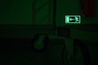 Photo luminescent evacuation sign (emergency exit door) on the wall. In the dark foreground stands two handling trucks.