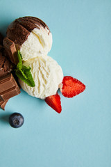 Wall Mural - top view of tasty brown and white ice cream with berries, chocolate and mint on blue background