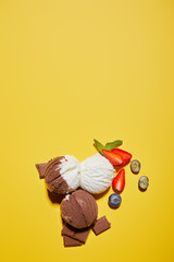 Wall Mural - top view of tasty brown and white ice cream with berries, chocolate and mint on yellow background