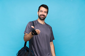 Wall Mural - Young sport man with beard over isolated blue background shaking hands for closing a good deal
