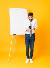 Wall Mural - Full-length shot of businessman giving a presentation on white board over isolated yellow background surprised and sending a message