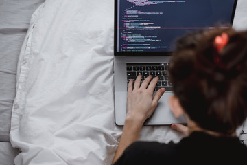 Young female programmer writes program code on a computer laptop in the bed at home. remote work