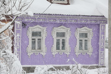 Wooden rural house with carved windows in winter. Snow, snowfall in countryside. Cold season, weather in village (Sergiyev Posad district, Moscow region, Russia). Russian folk style in architecture