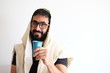 Bearded Jewish with a  Tallit (talis) and holding a cup of wine for the Kidush. The man is standing in front of a white background and has the Tallit covering his head