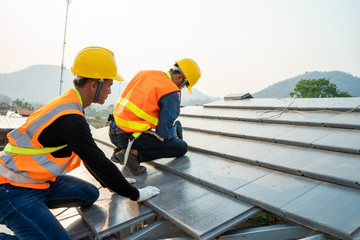 Poster - Roofer worker in special protective workwear and gloves installing new roof under construction residential building.