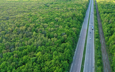 Wall Mural - Aerial view of a highway through a bright green forest. Straight road through the forest