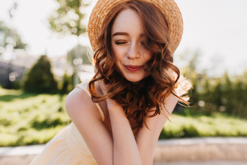 Relaxed ginger girl smiling with eyes closed. Outdoor photo of romantic red-haired woman in elegant hair posing on nature background.