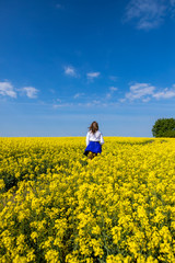 Wall Mural - young woman running in a field with yellow flowers, blue sky, space