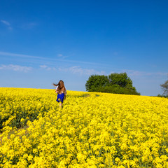 Wall Mural - young woman running in a field with yellow flowers, blue sky, space