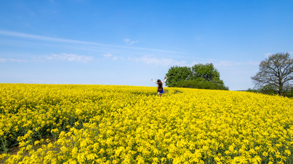 Wall Mural - young woman running in a field with yellow flowers, blue sky, space