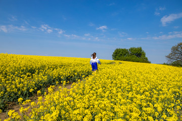 Wall Mural - young woman running in a field with yellow flowers, blue sky, space