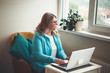 © Strelciuc - Thinking caucasian senior woman with blonde hair and eyeglasses working at the computer near the window during the quarantine