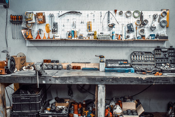 Moto workshop with hand tools. Workbench with sets of keys, screwdrivers, ploskobets, electrical tape, duct tape on the wall. Table with motorcycle parts, vise. Workspace for a joiner, auto mechanic