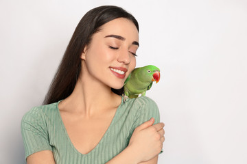 Wall Mural - Young woman with Alexandrine parakeet on light background. Cute pet