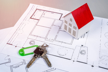 House model and keys lying on house blueprints on a desk. Real estate and construction industry concept.