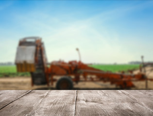 Empty wooden surface and blurred view of modern agricultural equipment in field. Space for text