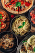 Table of italian meals on plates Pizza, pasta, ravioli, carpaccio, mushroom risotto, caprese salad and tomato bruschetta on rustic wooden background.
