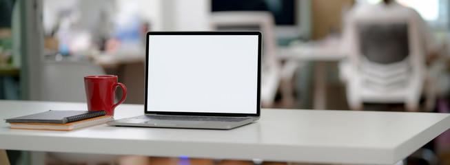 Cropped shot of simple office desk with blank screen laptop, mug, notebooks and copy space