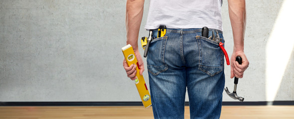 repair, construction and building - male worker or builder with level and working tools in back pockets over empty room of new home on background