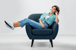 © Syda Productions - comfort, people and furniture concept - portrait of happy smiling young woman in turquoise shirt and jeans sitting in modern armchair over grey background