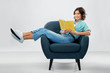 © Syda Productions - comfort, people and furniture concept - portrait of happy smiling young woman in turquoise shirt and jeans sitting in modern armchair and reading book over grey background
