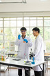 © jpixman30 - Science, Chemistry, Technology, Biology and Laboratory concept - Asian junior scientist is showing experiment result in glass beaker while Asian senior scientist gives a suggestion.
