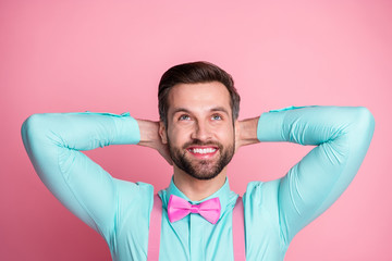 Wall Mural - Photo of handsome macho guy trend clothes outfit toothy beaming smile hold hands behind head look up empty space wear teal shirt suspenders bow tie isolated pastel pink color background