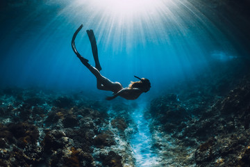 Wall Mural - Young freediver woman with fins glides and amazing sun rays. Freediving underwater in ocean
