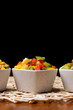 Vegetables in white bowls, diced on a brown kitchen table. Peppers, cucumbers, sweet corn and peas in a bowl on the table.
