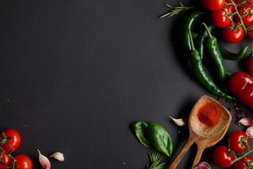 top view of organic cherry tomatoes, garlic cloves, fresh rosemary, peppercorns, basil leaves and green chili peppers on black