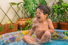 Boy Enjoying Summer In The Pool At Home. Boy Playing In The Kiddie Pool In The Backyard. Summer At Home Concept