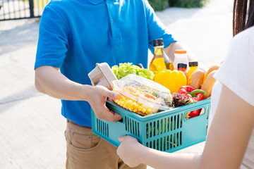 Wall Mural - Food Deliver Asian man in blue uniform give fruit and vegetable to receiver customer front house, fast express grocery service when crisis coronavirus, covid19 new normal lifestyle concept.