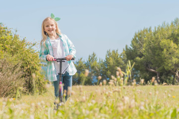 Active little toddler girl riding scooter on road in park outdoors on summer day.  Summer time fun