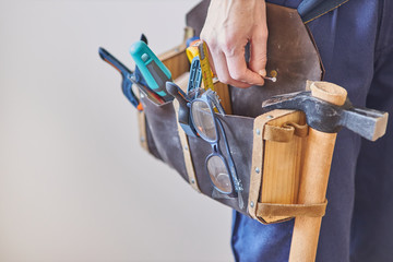 Carpenter's belt with tools. Woman's hand taking a wood nail. Unrecognizable person