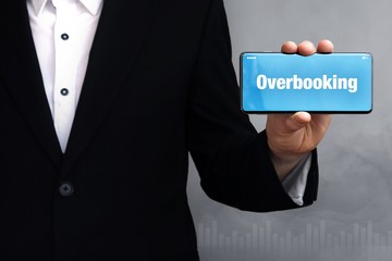 Wall Mural - Overbooking. Businessman holding a phone in his hand. Man present screen with word. Blue Background. Business, Finance, Statistics, Analysis, Economy