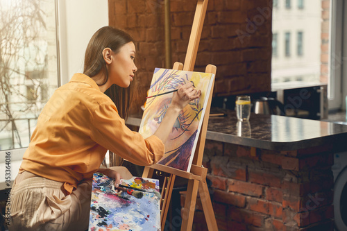 Cuadros en Lienzo Pretty lady painting beautiful picture on easel at home