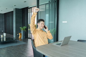 Portrait of happy smiling young business Asian, Chinese man person using laptop computer, working, and talking on smart mobile phone in meeting room at home in technology device concept. Lifestyle