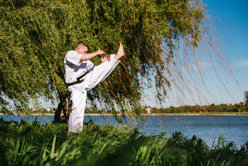 A man karate fighter in white kimono training outdoor in the park