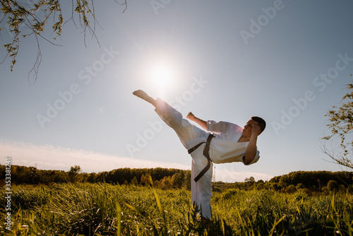 A silhouette of man karate fighter in white kimono high kick on the sunset background