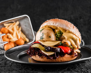 Canvas Print - Vegetarian burger with cheese, zucchini, tomatoes, lettuce, mushrooms and fried stick balls, french fries on slate black background, close up