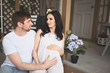 © Алина Троева - Pregnancy and people concept - happy man hugging his beautiful pregnant wife at home. Future parents waiting unborn baby. Love, relationship, birth, happy family concept - young lovely married couple