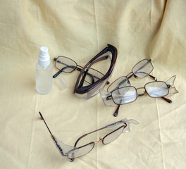 A top down view of various pairs of glasses and safety glasses along with a spray bottle of glass cleaner.