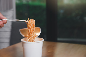 Hand of a man holding a plastic fork with cooked instant noodles. A cup of instant noodle with fork ready to eat convenient and delicious food.